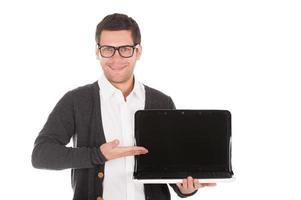 Pointing a copy space. Cheerful young man holding a laptop and pointing a monitor while standing isolated on white photo