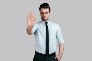 No way to cheat him Serious young man in white shirt and tie gesturing and looking at camera while standing against grey background photo