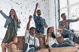 totalmente despreocupado. grupo de jóvenes felices con ropa informal bebiendo champán mientras hacen una fiesta con confetti volando por todas partes foto