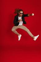 Full length of playful young man in casual clothing making a face and punching while hovering against red background photo