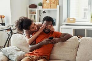 Playful young African woman covering eyes to her boyfriend while spending time at home