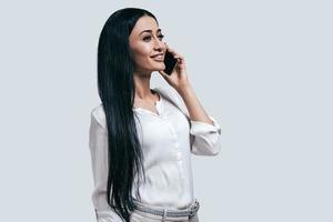 Business arrengments on the phone. Young business woman talking on the phone and smiling while standing against grey background photo