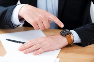 Time is money. Close-up of businessman pointing on his watch while sitting at his working place photo