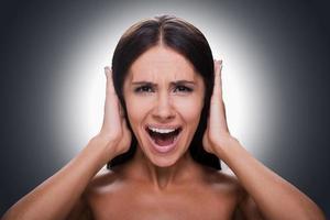 Too loud sound Portrait of frustrated young shirtless woman shouting and covering ears by hands while standing against grey background photo