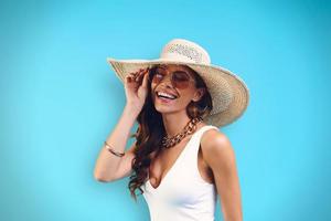 Portrait of beautiful young woman in elegant hat looking at camera while standing against blue background photo