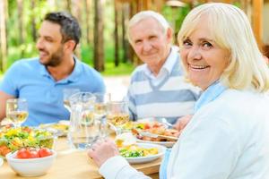 Proud to have a big family. Happy family sitting at the dining table outdoors while senior woman looking over shoulder and smiling photo