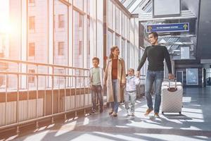 toda la longitud de una familia feliz con dos niños pequeños caminando por la terminal del aeropuerto foto