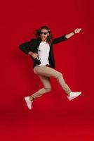 Full length of playful young man in casual clothing smiling and playing imaginary guitar while hovering against red background photo