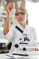 The formula is almost complete. Beautiful young female scientist holding test tube and looking at it while working in the laboratory photo