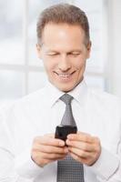 Businessman with mobile phone. Cheerful senior man in shirt and tie holding mobile phone and looking at it with smile photo