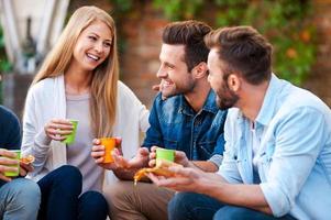 Quality time with best friends. Group of happy young people talking to each other and eating pizza while sitting outdoors photo