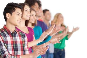 Applause. Group of cheerful young multi-ethnic people standing in a row and applauding to someone while standing isolated on white photo