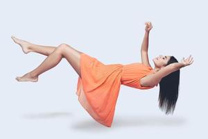 Flying so high. Full length studio shot of attractive young woman in orange dress hovering in air and keeping eyes closed photo