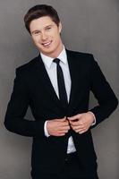 Making business look good. Handsome young man in formalwear adjusting his jacket and smiling while standing against grey background photo