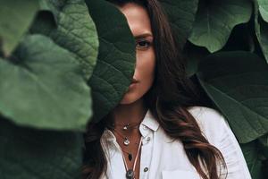Naturally beautiful. Close-up of young woman looking at camera while standing among the leaves outdoors photo