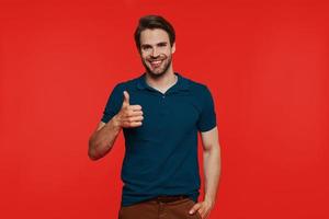 Happy young man in casual wear looking at camera and showing his thumb up photo