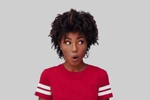 Surprised young African woman looking away and smiling while standing against grey background photo