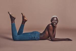 Smiling beauty. Attractive young African woman looking away and smiling while lying against brown background photo