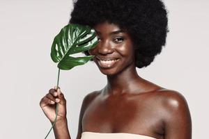 retrato de una hermosa joven africana sosteniendo una planta cerca de la cara y sonriendo foto