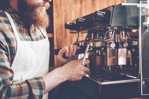 Making best coffee. Side view close-up part of bearded man in apron making coffee while standing at cafe photo