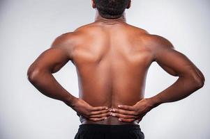 Backache. Rear view of young muscular African man touching his hip while standing against grey background photo