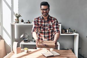 Gift for you Handsome young man giving a gift box and looking at camera with smile while standing in the creative working space photo