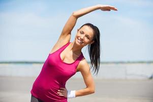 Doing stretching exercises. Beautiful young woman doing stretching exercises while standing outdoors photo