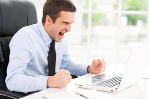 Failed again. Furious young man in shirt and tie looking at computer monitor and shouting while sitting at his working place photo