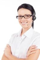 Customer service representative. Confident young woman in headset smiling and keeping her arms crossed while standing isolated on white photo