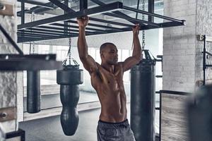 Full of energy. Handsome young African man doing pull-ups while exercising in the gym photo