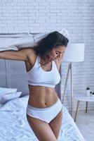 Sensual moment. Attractive young woman in underwear taking off her T-shirt  and keeping eyes closed while standing in the bedroom 13503209 Stock Photo  at Vecteezy