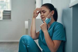 Stressed young female nurse in protective face mask crying while working in the hospital photo