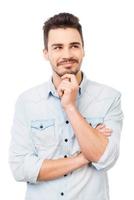 Up with a plan. Thoughtful young man in shirt looking away and holding hand on chin while standing against white background photo