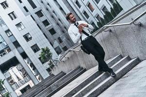 en el camino a la reunión de negocios. toda la longitud de un joven con traje completo sonriendo mientras camina al aire libre foto