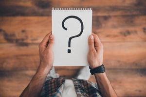 Searching for answers. Top view of man holding note pad with question mark on it while standing on the wooden floor photo