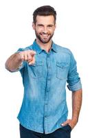 Choosing you. Confident young handsome man in jeans shirt pointing you and while standing against white background photo