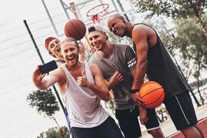 creando recuerdos felices. grupo de hombres jóvenes en ropa deportiva tomando selfie y sonriendo mientras están de pie al aire libre foto