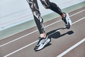 Determined to win. Close up of young woman in sports shoes jogging while exercising outdoors photo