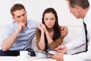 Expert advice. Thoughtful young couple sitting on the couch while confident financial advisor explaining something and pointing clipboard photo