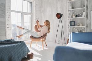 Effortless beauty. Beautiful young woman taking selfie using smart phone while sitting in the armchair at home photo