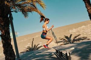 Achieving best results. Full length of beautiful young woman in sports clothing jumping while exercising outdoors photo