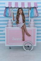 Ready to sell candies.  Cute little girl looking at camera and smiling while sitting on the candy cart decoration photo