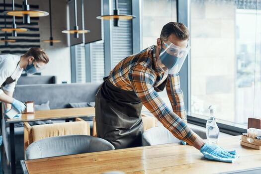 dos jóvenes camareros en ropa de trabajo protectora limpiando mesas en el restaurante foto