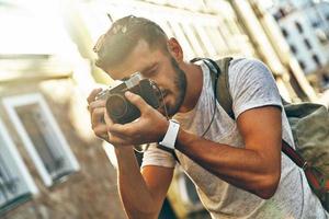 Handsome young man in casual clothing photographing with digital camera while standing outdoors photo