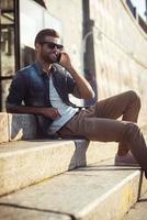 How are you Low angle view of happy young man talking on the mobile phone while sitting on stairs photo