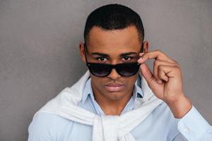 Well hello Confident young African man adjusting his sunglasses and looking at camera while standing against grey background photo