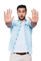 Stop it Terrified young Indian man stretching out hands and staring at you while standing against white background photo