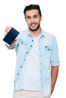 Look at my new smart phone Handsome young Indian man showing his smart phone and smiling while standing against white background photo