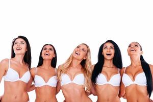 Wow Group of beautiful young women in lingerie embracing and looking up with smiles while standing against white background photo