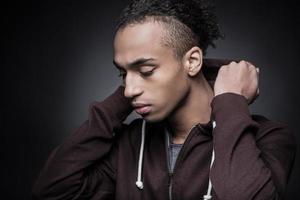 In his own style. Side view of young Africanman putting the hood on while standing against black background photo